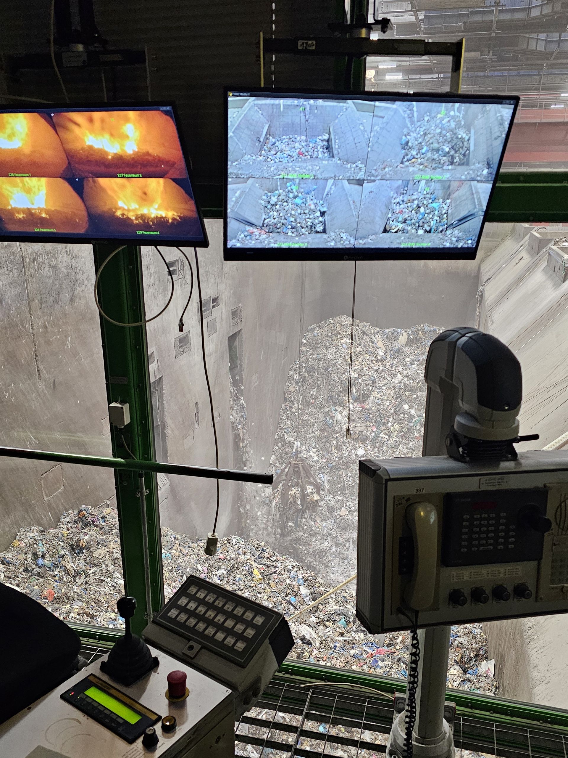 Blick aus der Krankanzel in den Restmüllbunker, im Vordergrund verschiedene Bildschirme mit Informationen 