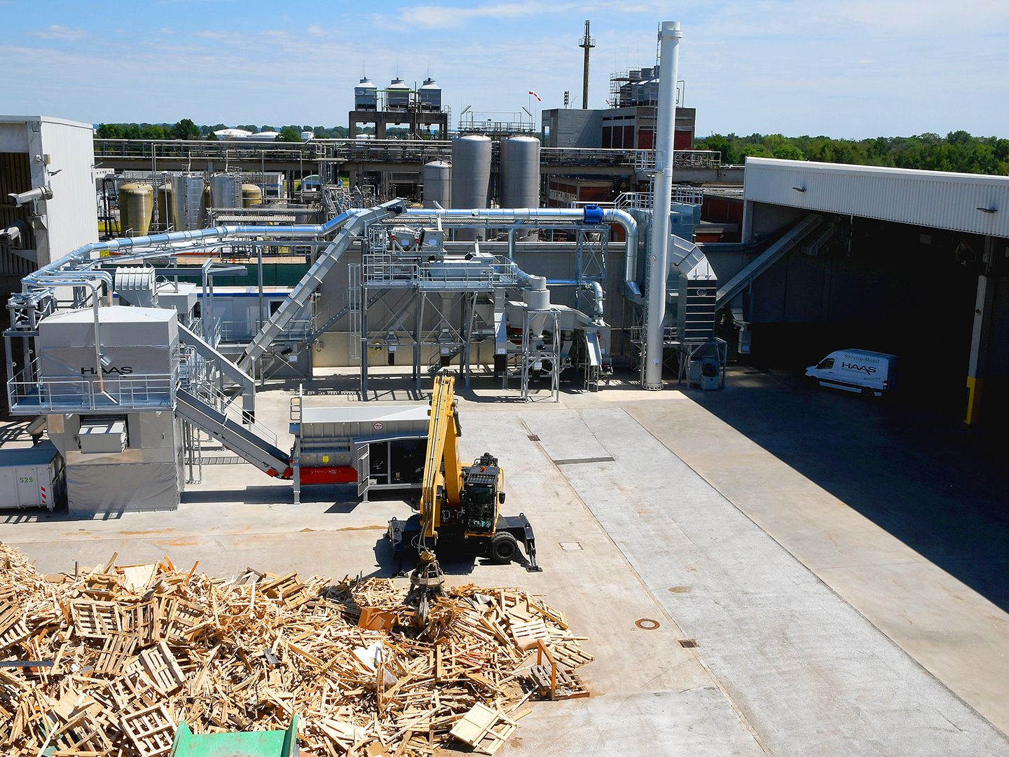 Altholzaufbereitungsanlage mit losem Holzlager und Bagger bei der Verarbeitung von Altholz.