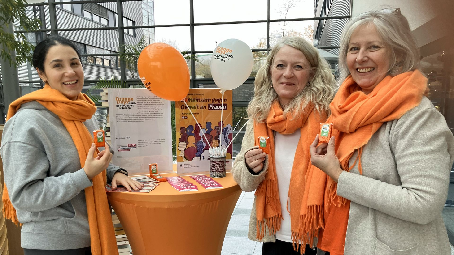 Drei Frauen mit orangenen Schals, werben für den Orange Day 
